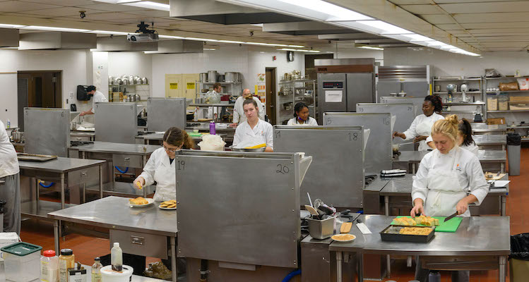commercial kitchen with culinary arts students preparing food dishes