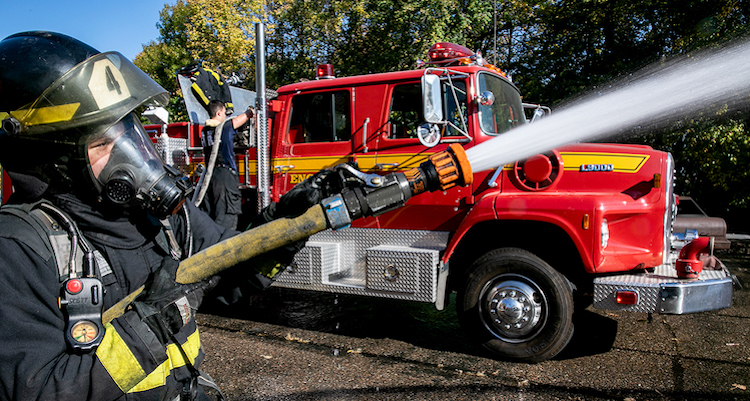 fire fighter in uniform holding fire hose standing next to a fire truck