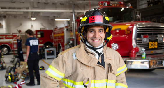 fire fighter in uniform holding fire hose standing next to a fire truck