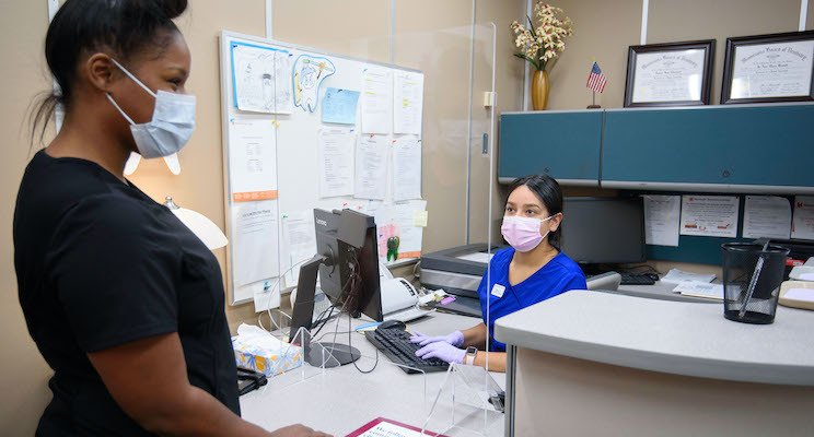 patient talking to a healthcare worker behind plexiglass and desk