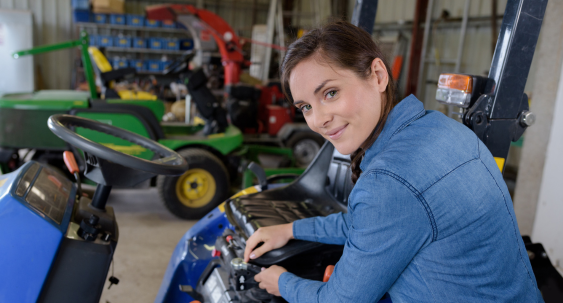 female working on a riding lawnmower in a shop