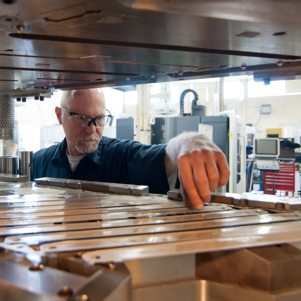 Woman in coveralls writing at a plumbing workbench with tools and pipe fittings.