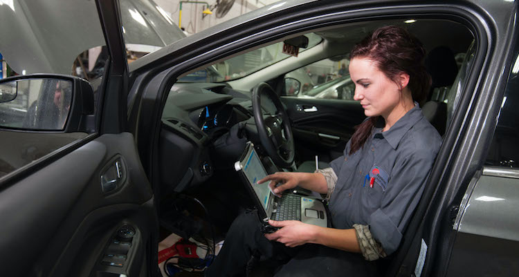 female automotive technology student with laptop running diagnostics inside of a car