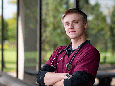 male healthcare student posing outside with stethescope and maroon scrubs