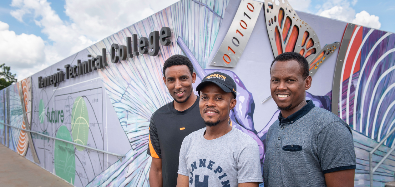 three male students standing by mural at entrance