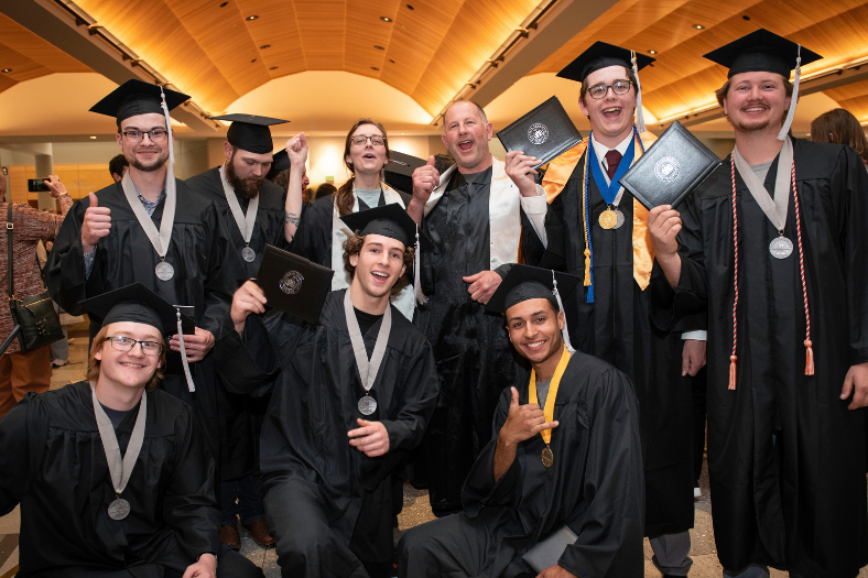 A group of HVAC students and staff pose in their caps and gowns at their graduation ceremony. Students hold their diplomas.