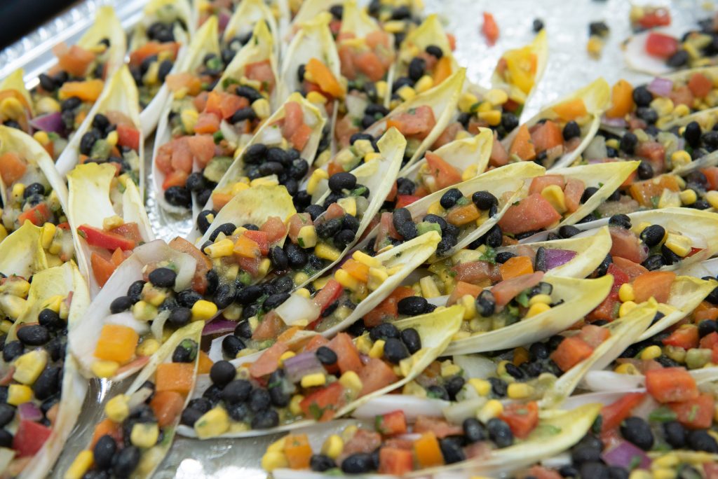 Endive leaves filled with a colorful mixture of black beans, corn, diced tomatoes, red onion, and bell peppers showcase the artistry of culinary arts, beautifully arranged by the chef on a silver tray.